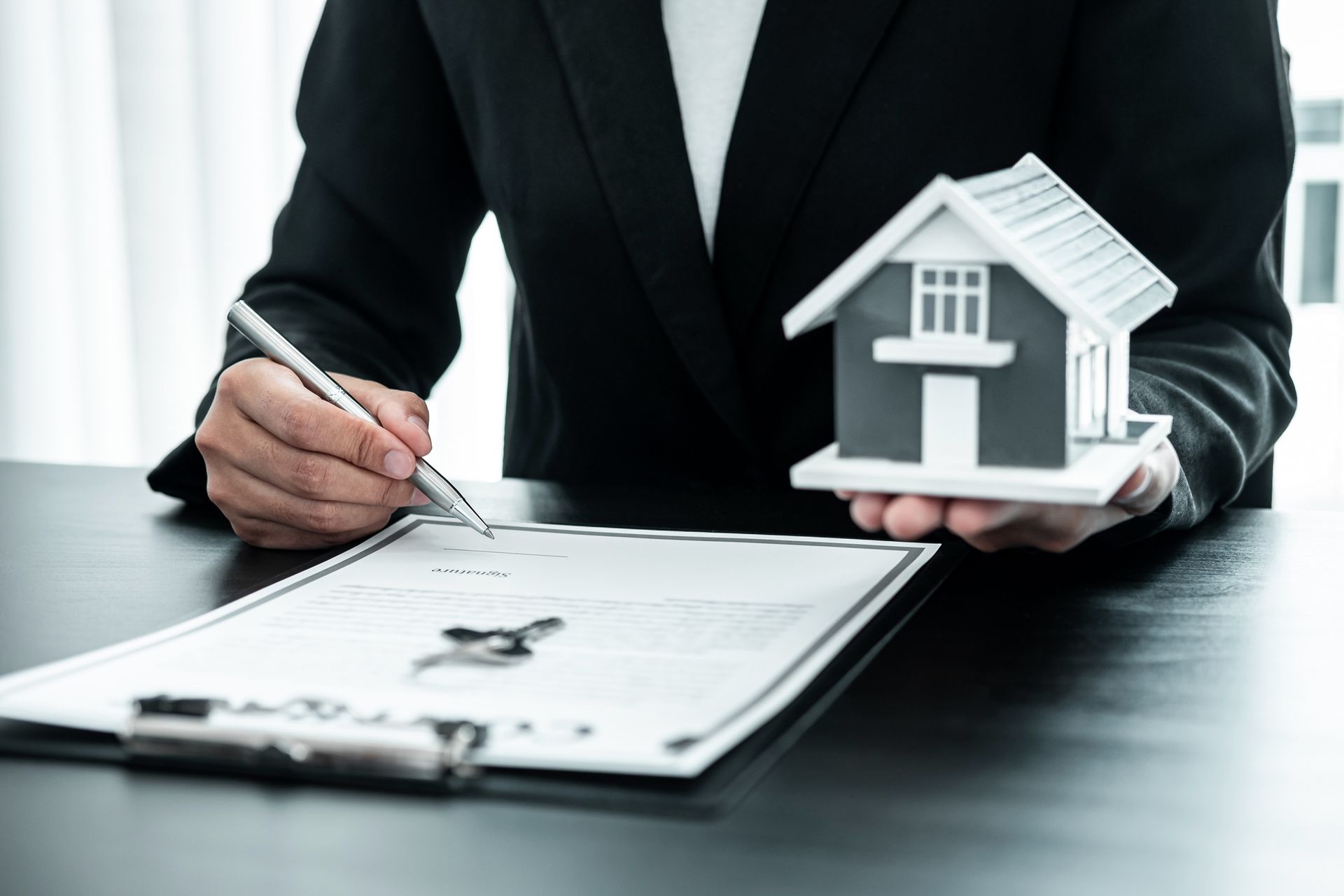 Real estate agent signing property contract while holding a house model on desk. Real estate agent signing property contract while holding a house model on desk.