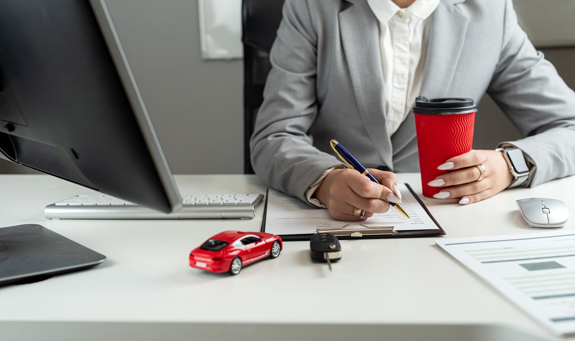 Auto insurance provider writing policy paperwork at desk with coffee, toy car, and car key