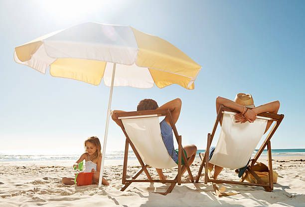 A family is sitting in lawn chairs under an umbrella on the beach.