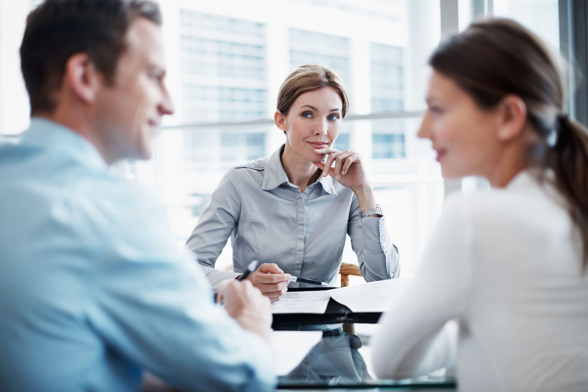 Consultant sits in front of couple inside a business insurance agency as she looks at the camera.