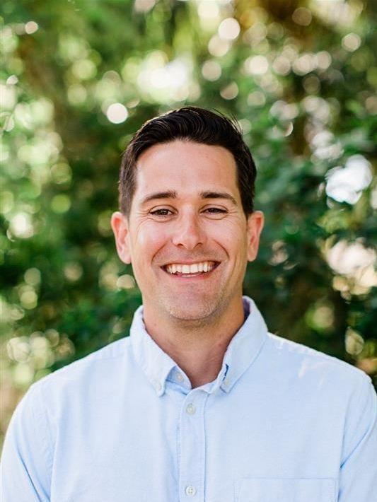 A man in a blue plaid shirt is standing in front of a plant.