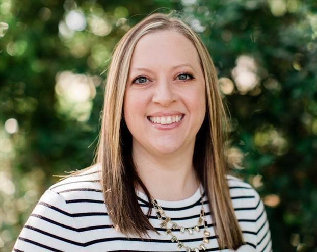 A woman in a red dress and black sweater is smiling for the camera.