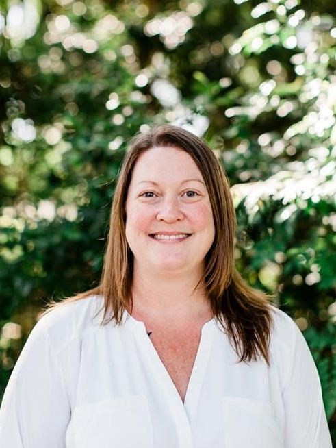 A woman wearing a purple shirt and a necklace is smiling for the camera.