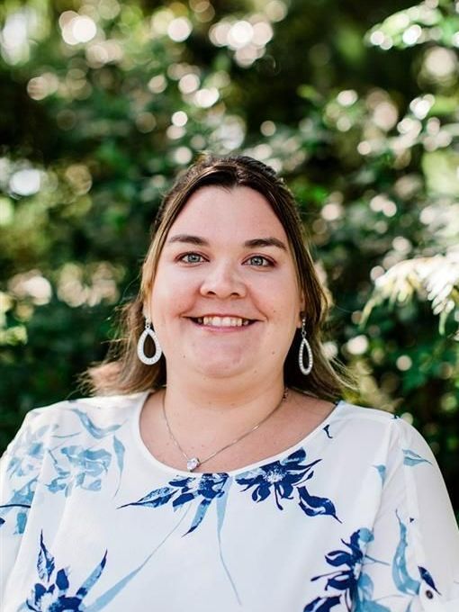A woman wearing a purple shirt and a necklace is smiling for the camera.