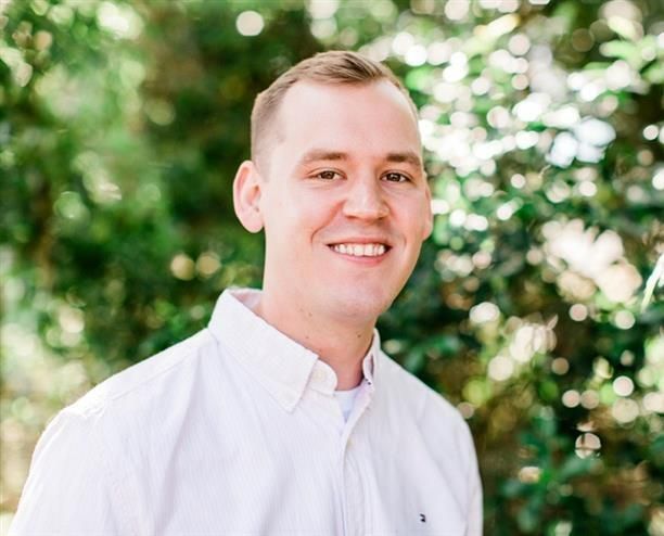 A woman wearing a blue shirt and a black sweater is smiling for the camera.