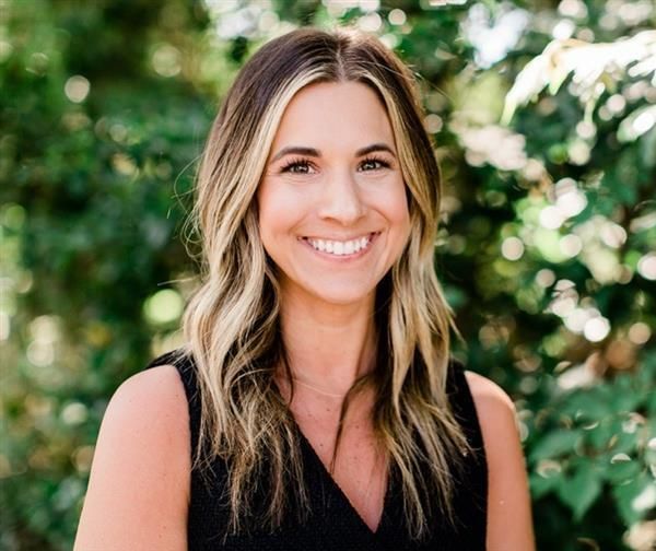 A woman wearing a black tank top and a gold chain is smiling for the camera.
