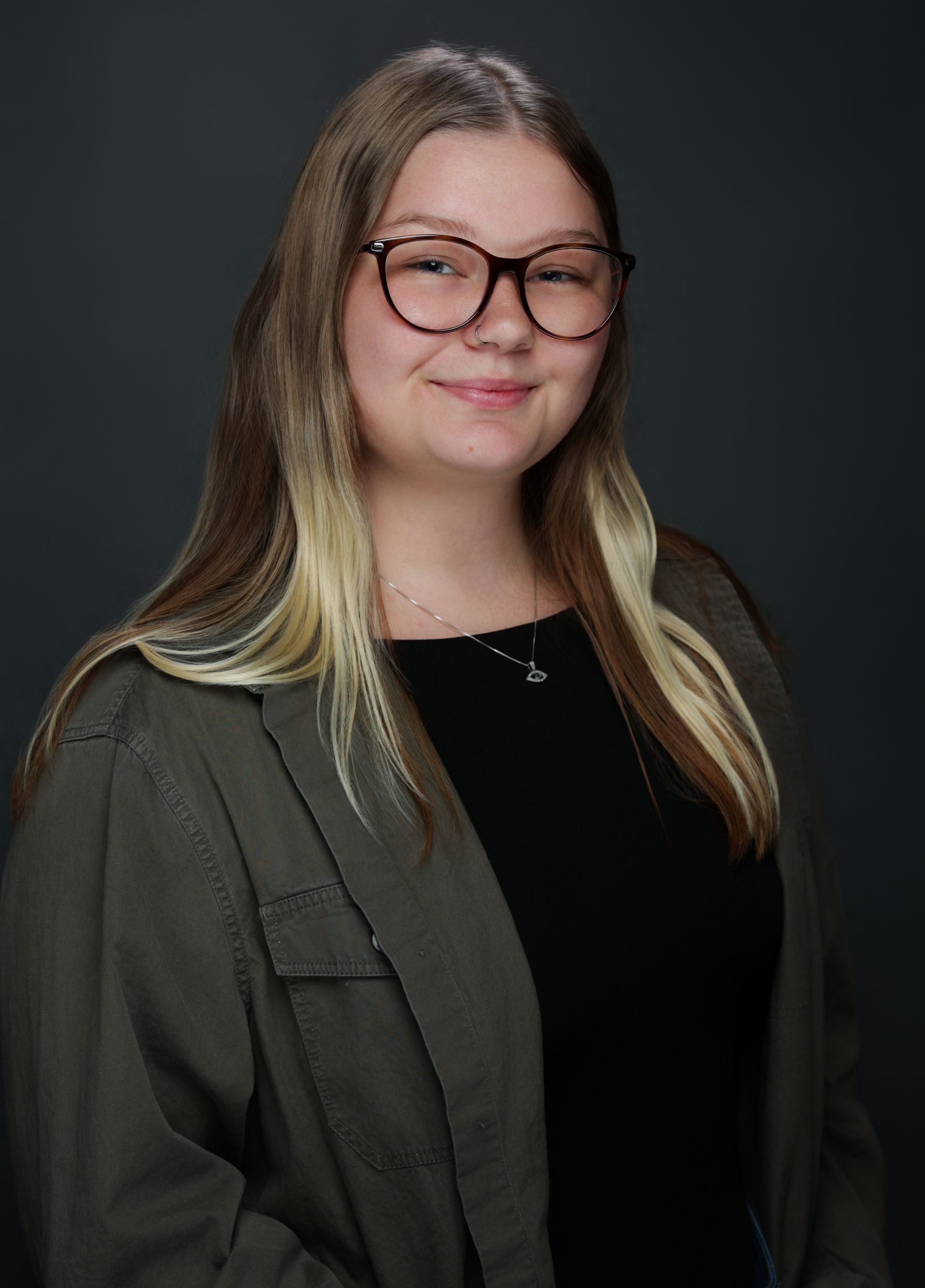 A woman wearing glasses is standing in front of a painting.