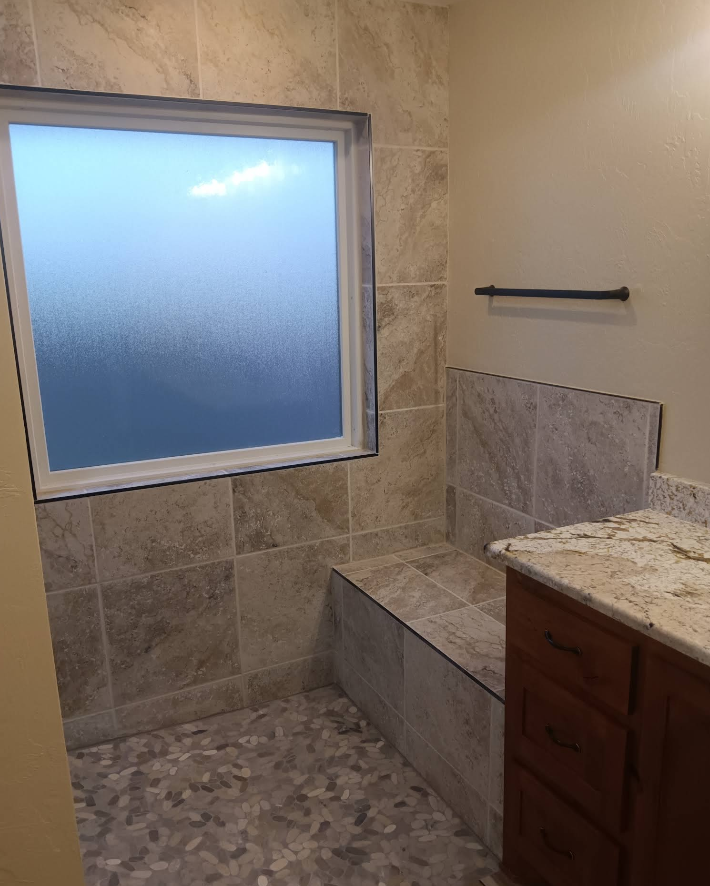 Bathroom with tiled shower bench, window, and vanity with granite countertop.