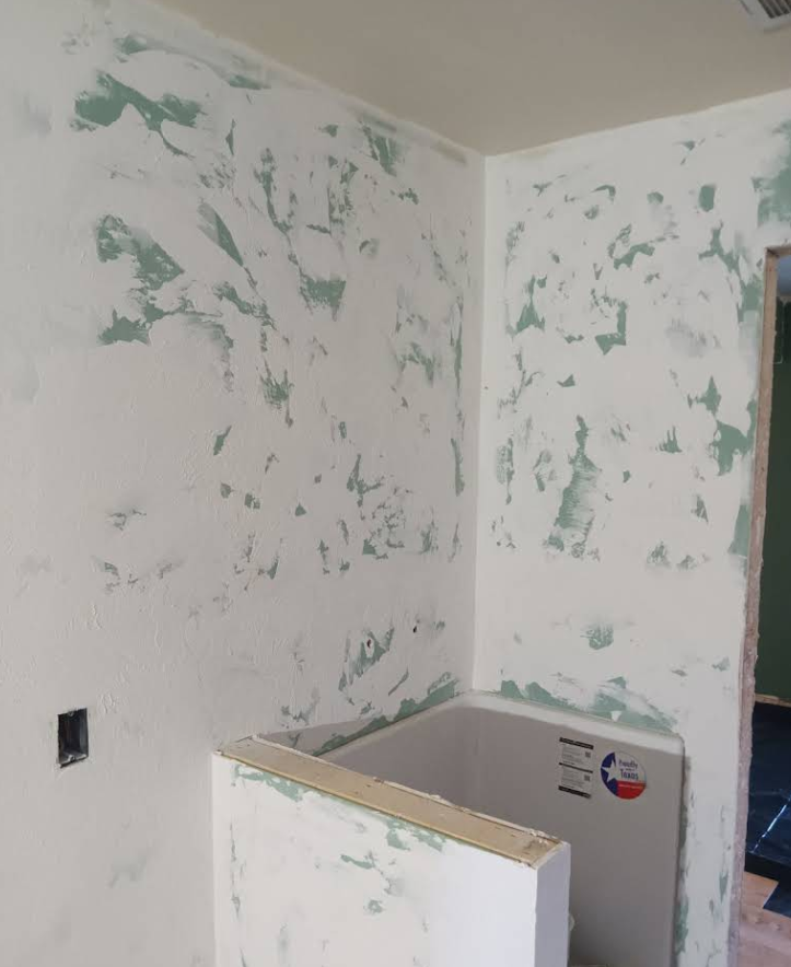 Walls with white compound over green. Corner of a room with a bathtub.