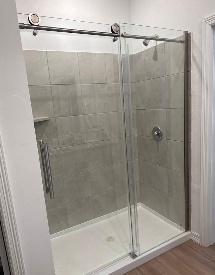 Glass shower enclosure with sliding door and gray tiled walls.