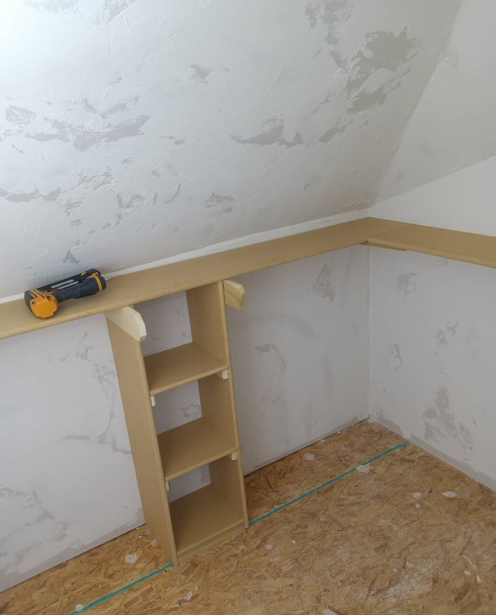 Built-in shelf unit in a room with angled ceiling and exposed subfloor. A level sits on a horizontal beam.