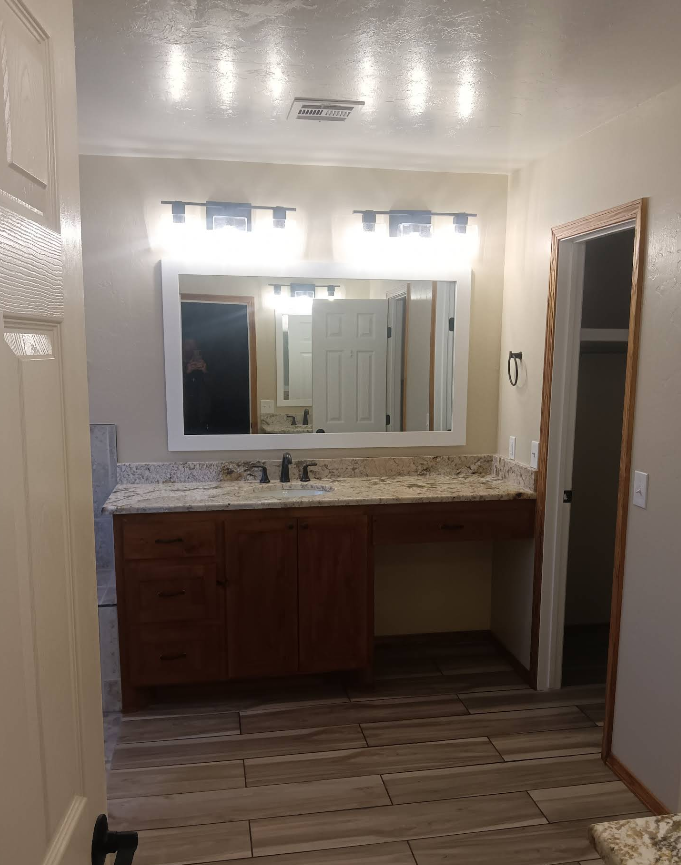 Bathroom with wood vanity, granite countertop, large mirror, and bright lighting.