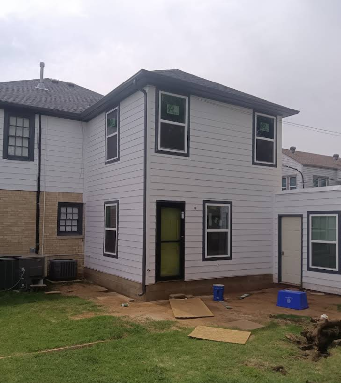Two-story house with white siding and dark trim. New windows installed. Construction in progress.