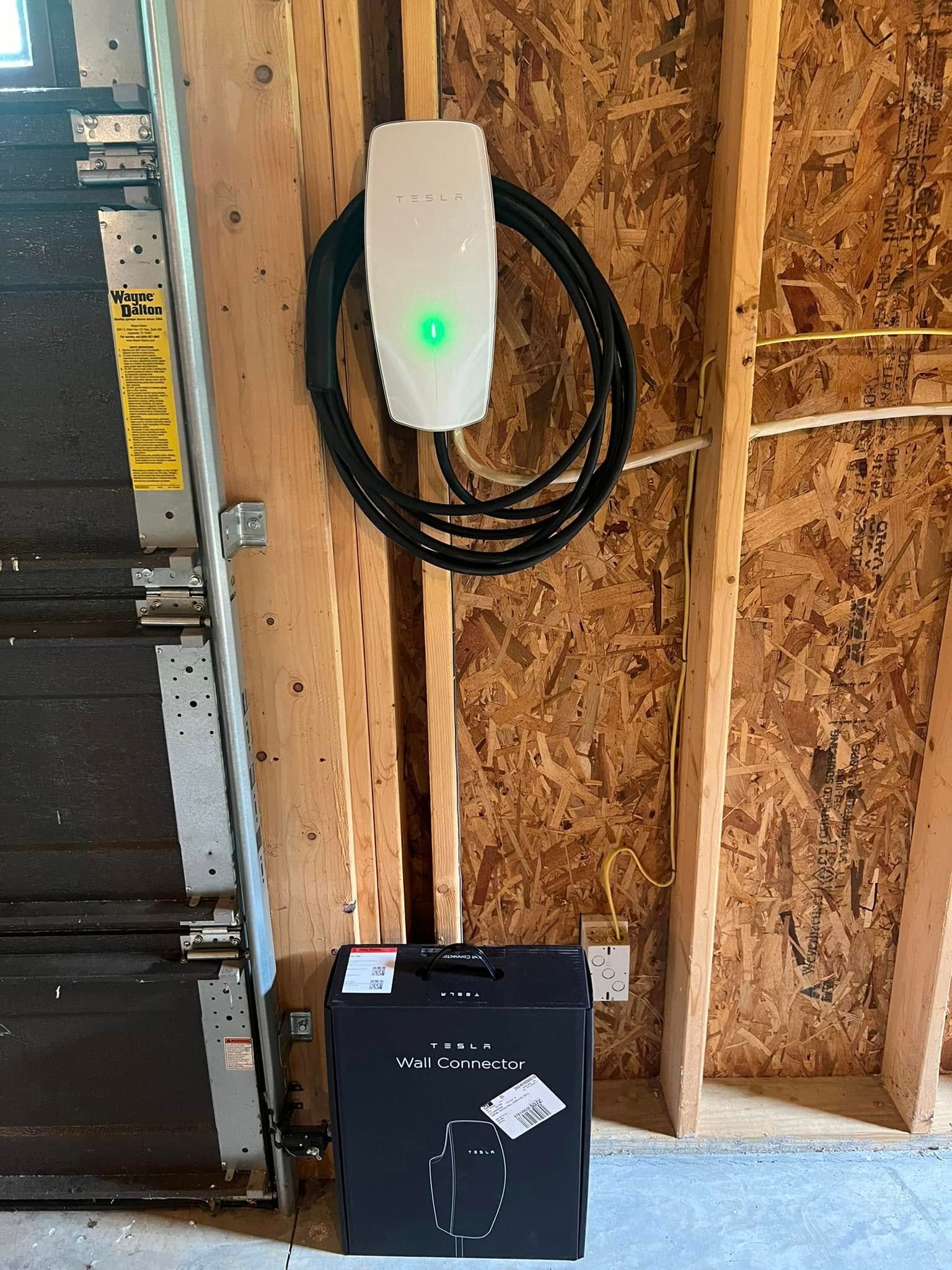 A tesla charging station is hanging on a wall next to a garage door.