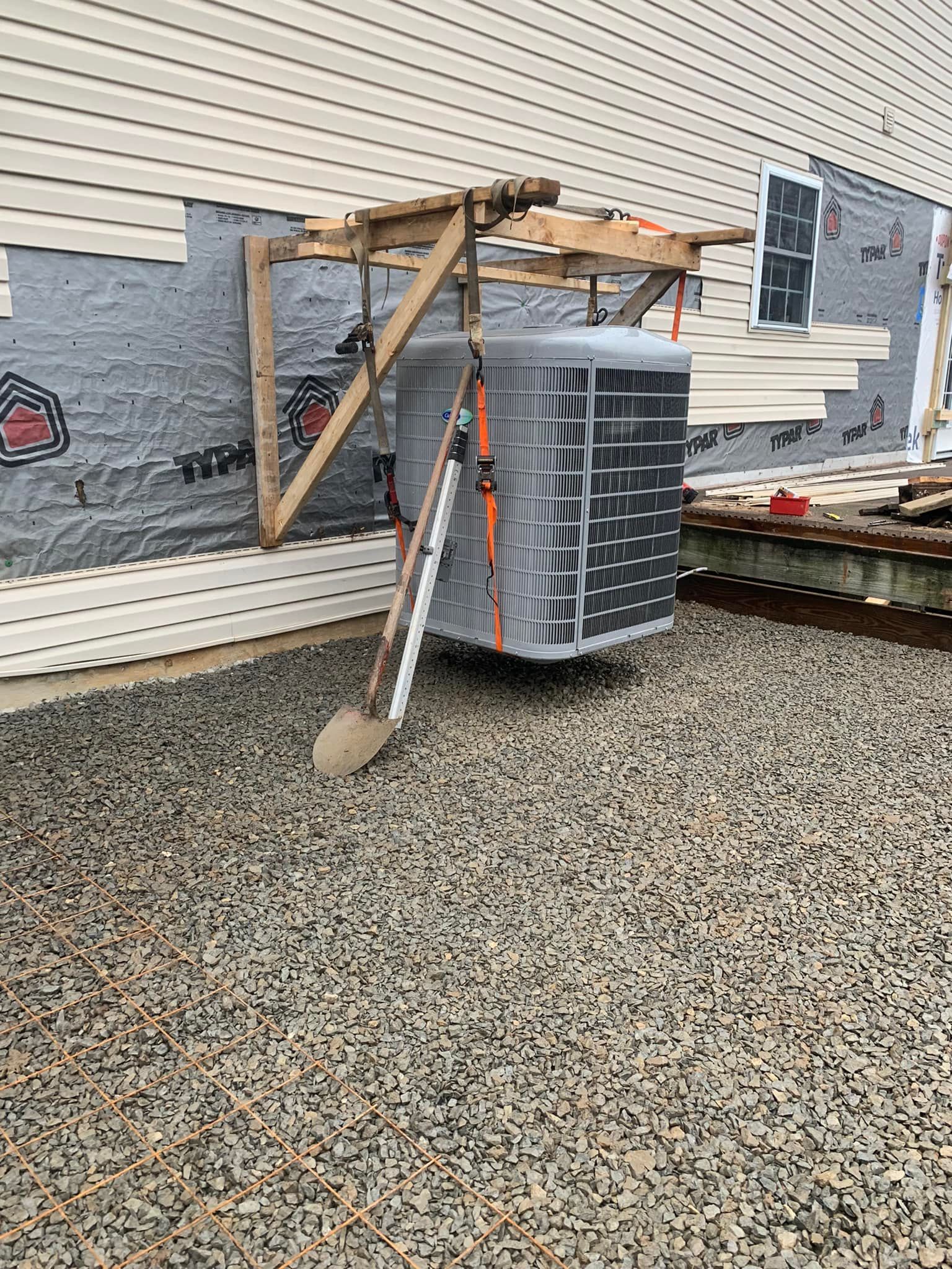 A large air conditioner is sitting in front of a house under construction.