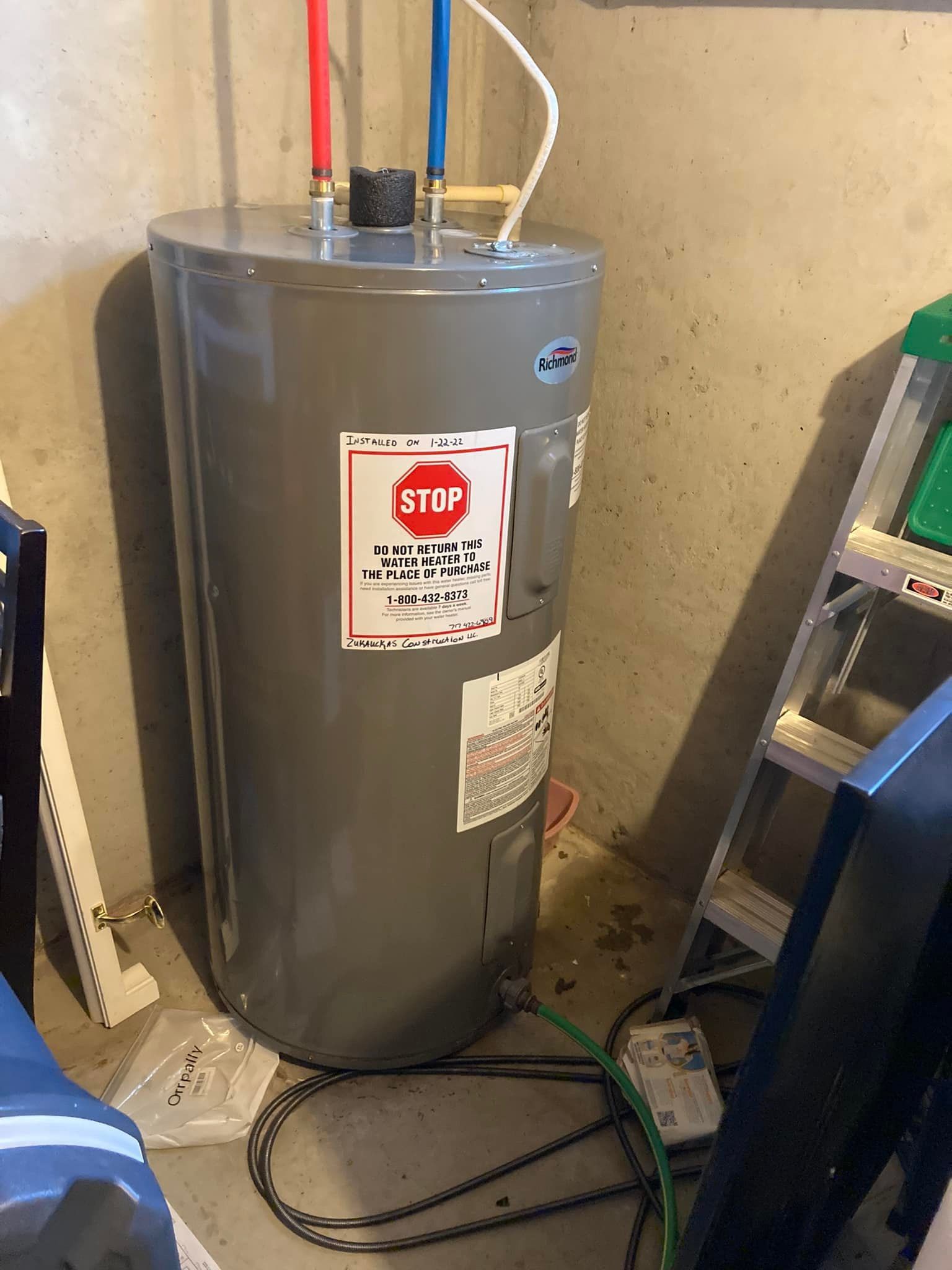 A water heater is sitting in a room next to a ladder.