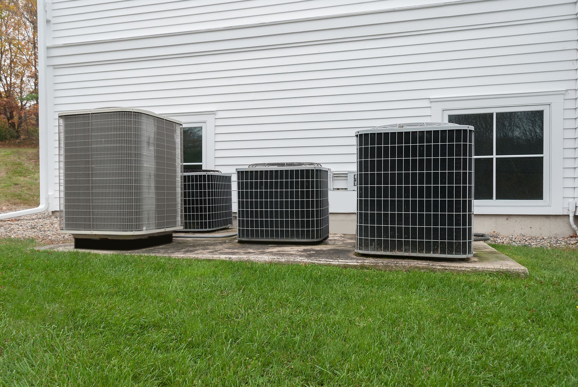 A row of air conditioners are sitting in front of a white house.