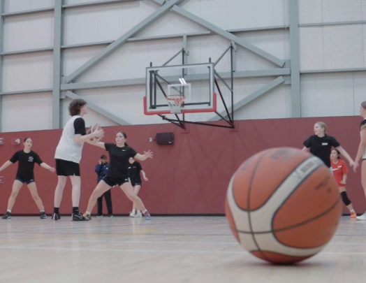 Basketball practice in a gym, with players near the hoop and a ball in the foreground.