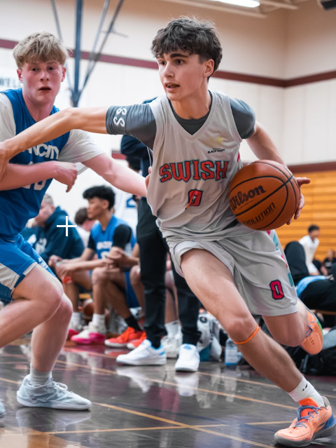Basketball player in gray jersey dribbles past a defender during a game on a gym court