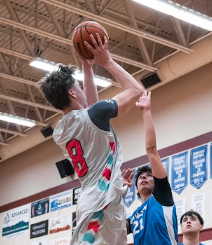 Basketball player in gray jersey leaps for a shot over a defender in blue during an indoor game