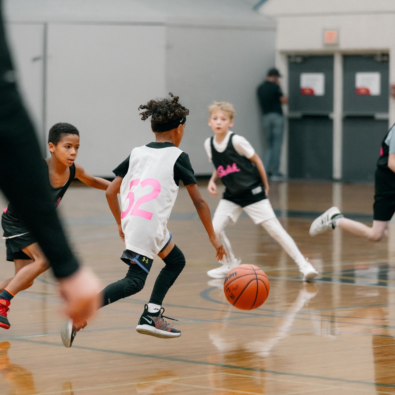 Youth basketball game in a gym, with players dribbling and defending around a loose orange ball.