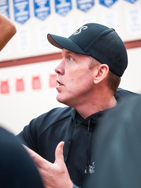 Man in a black cap speaking indoors, gesturing with his hands during a discussion.