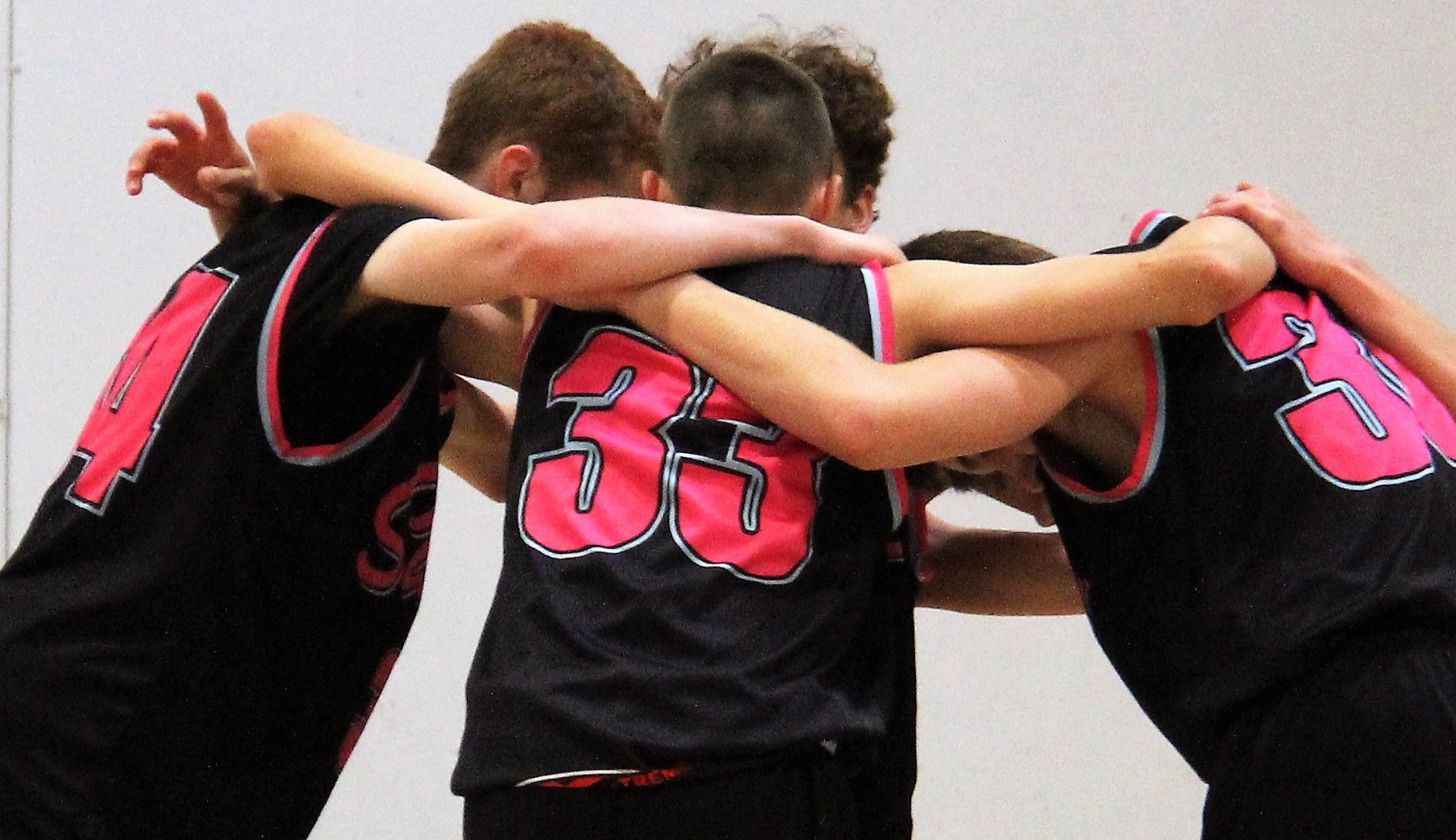 Three players in black jerseys with pink numbers huddle with arms around each other