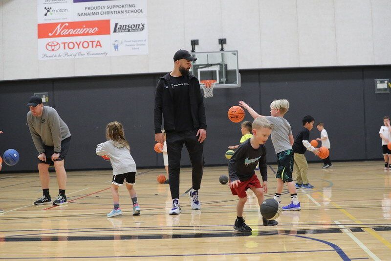 Children and an adult dribble basketballs during a gym practice on an indoor court