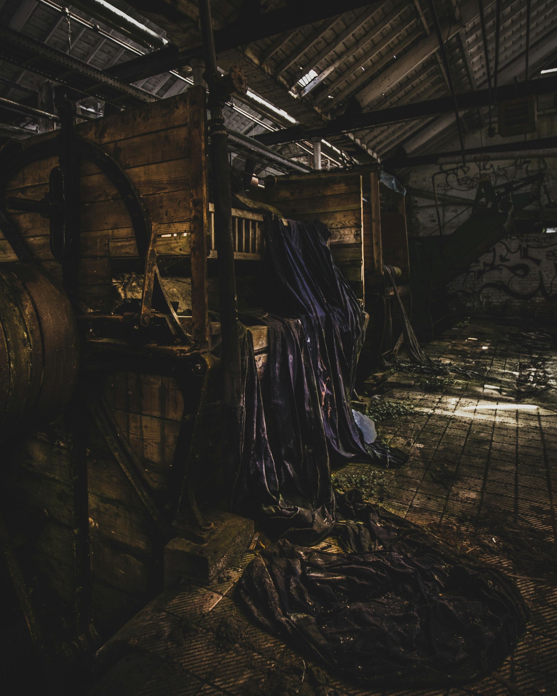 Dark, weathered interior of an abandoned wooden structure. Dark blue fabric hangs from the dilapidated beams.