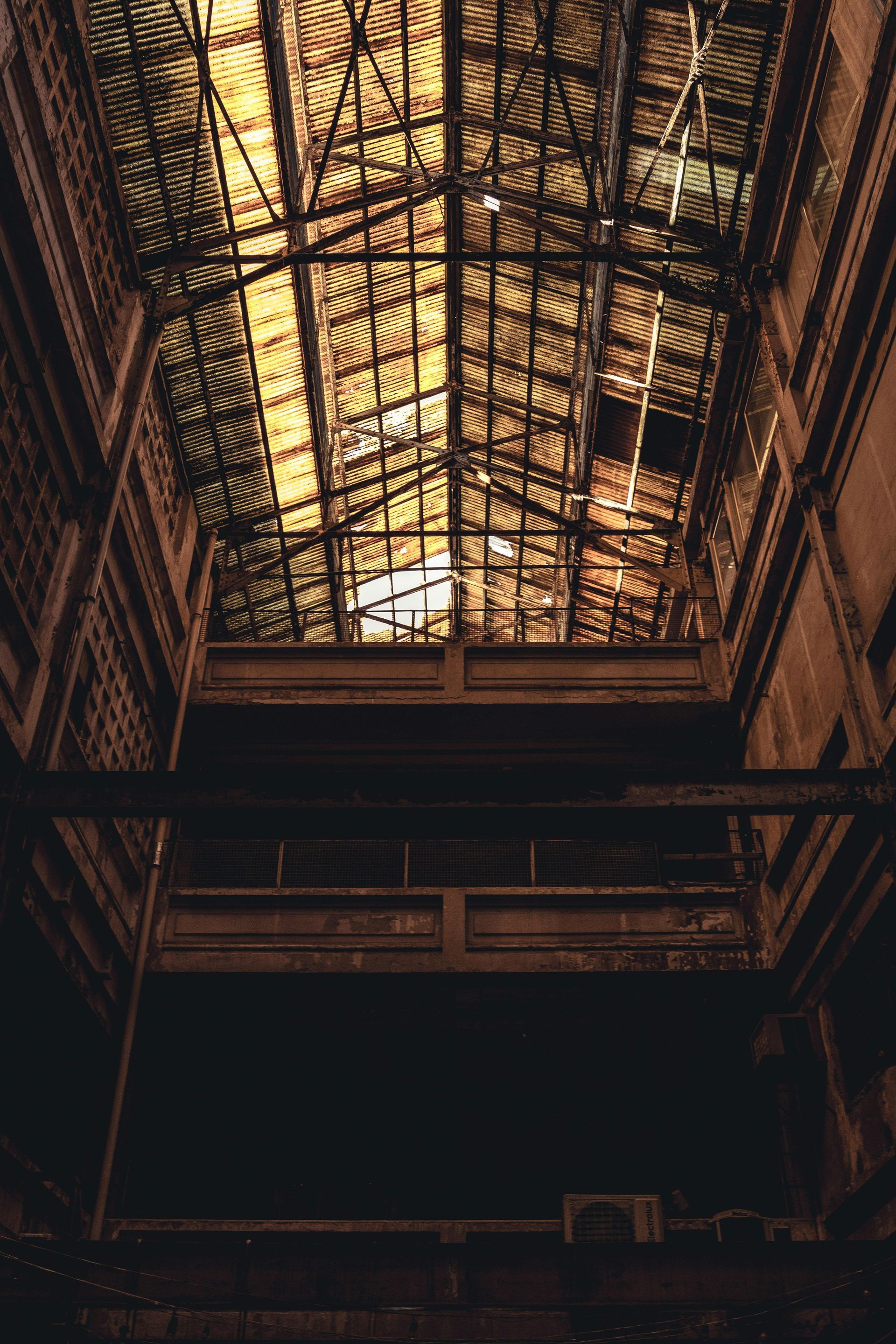 Interior view of a dilapidated industrial building, looking up at a deteriorating glass and metal roof.