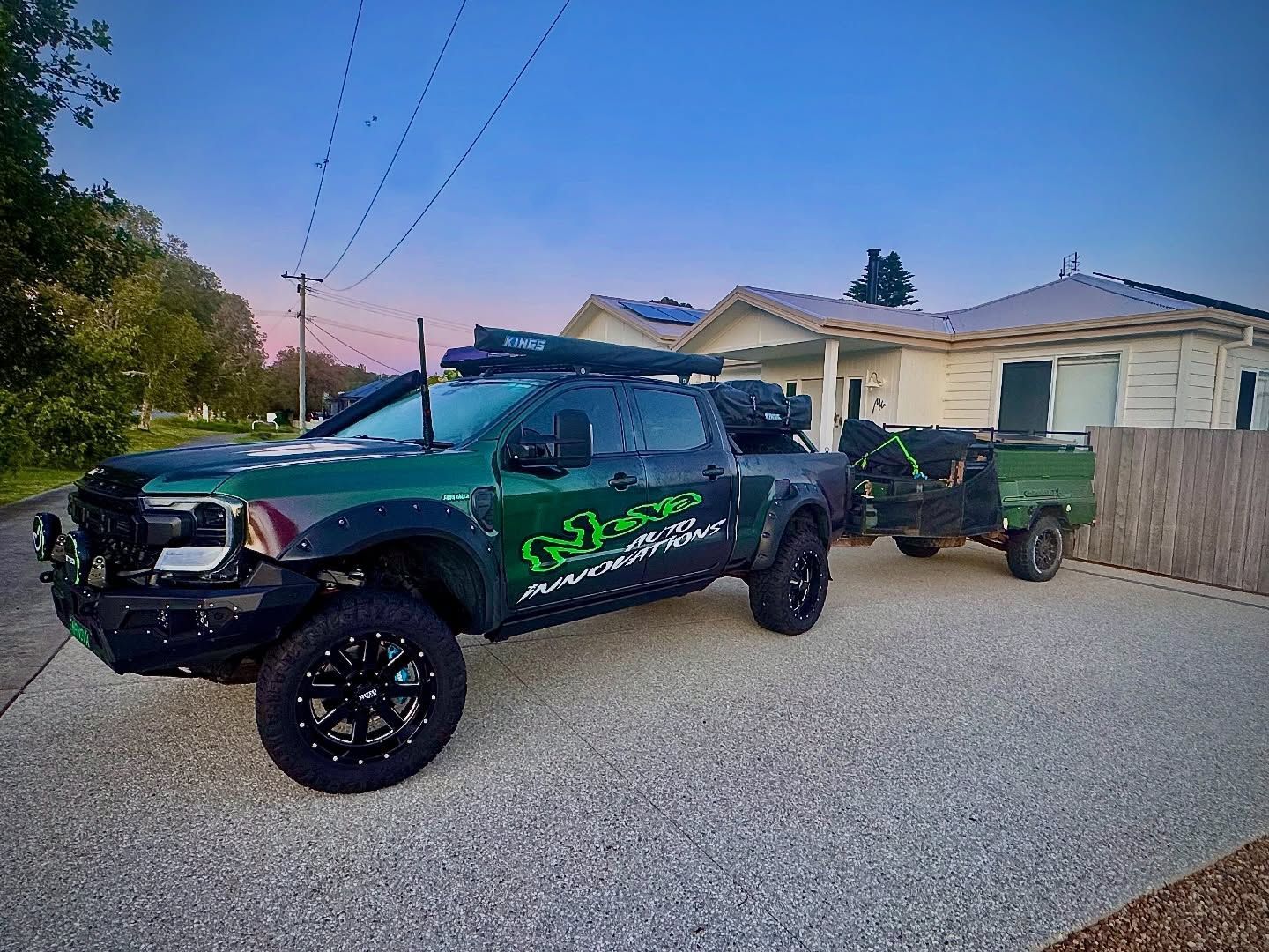 A dark green, modified pickup truck with large tires and decals, parked in a residential driveway while towing a trailer  — Nova Auto Innovations in Charlestown, NSW