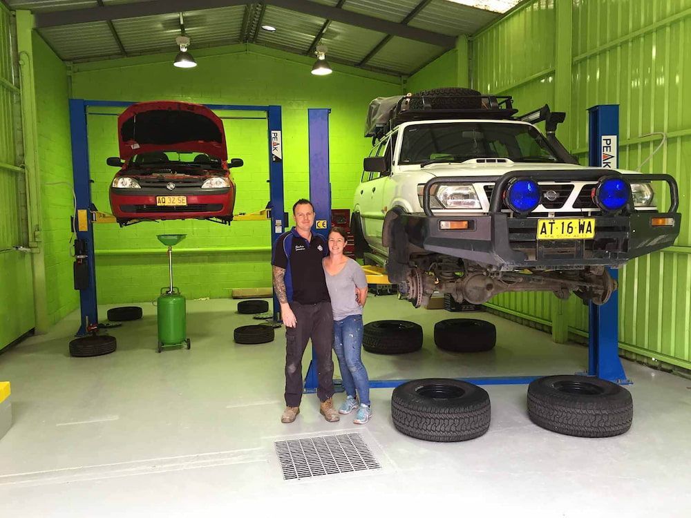 Couple Standing in a Green Garage With Cars on Lifts, Surrounded by Tires — Nova Auto Innovations in Charlestown, NSW