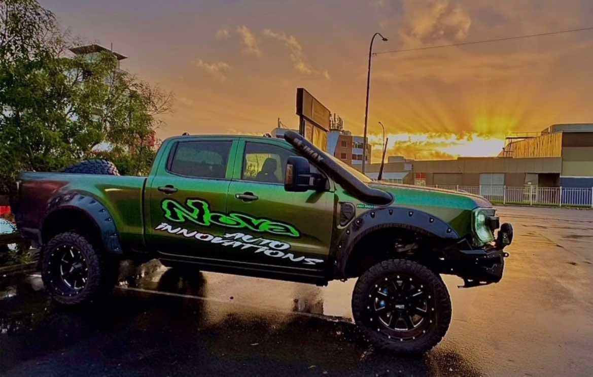 Green lifted pickup truck with black rims and snorkel, parked at sunset.