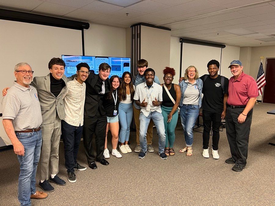 Group of people smiling, standing together in a room with screens and a flag.
