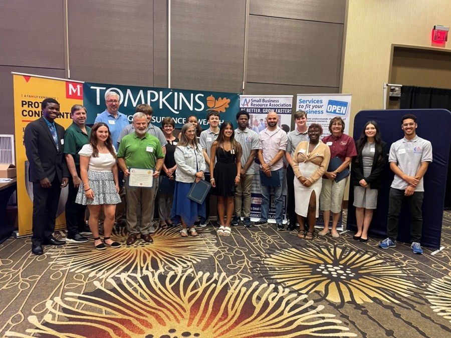 Group of people standing together, possibly at an event, with banners in the background.