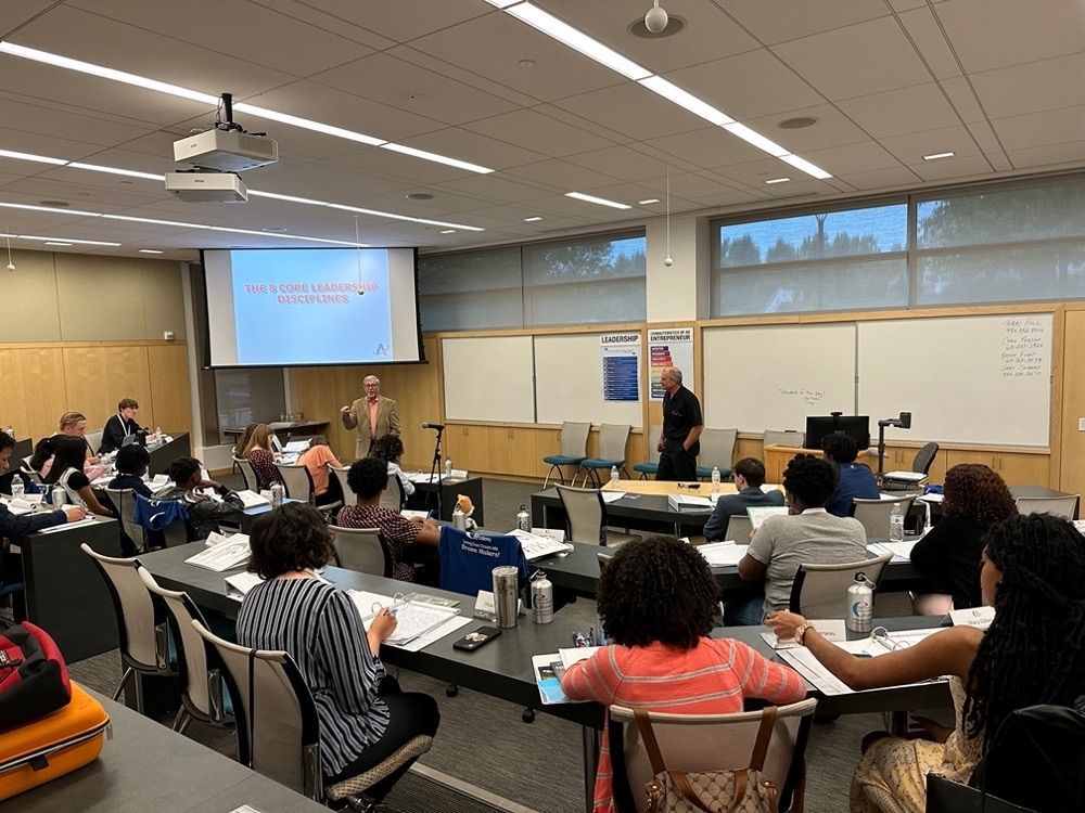Classroom presentation with two speakers; students taking notes at desks.