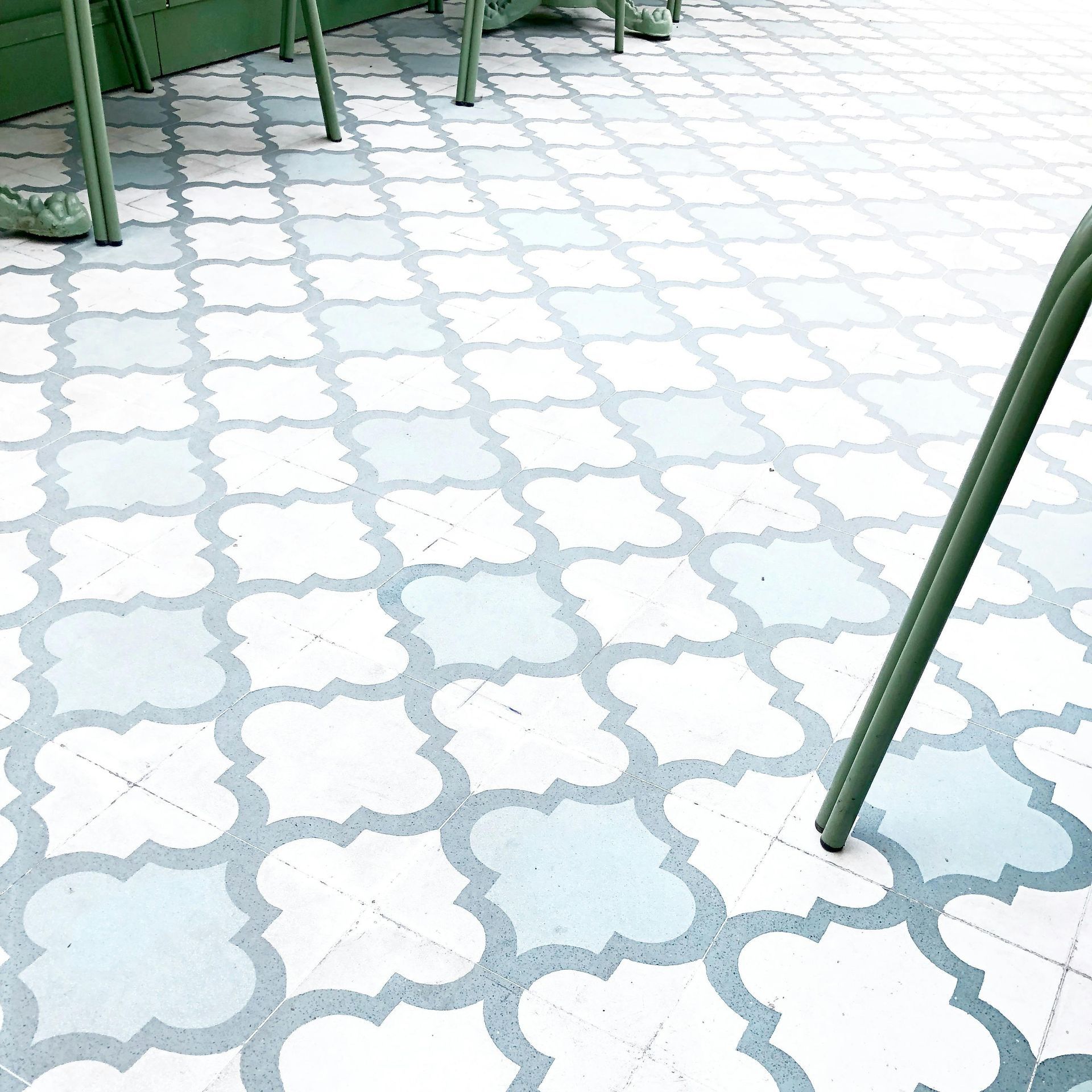 Green chair legs on patterned, light blue and white tile floor.