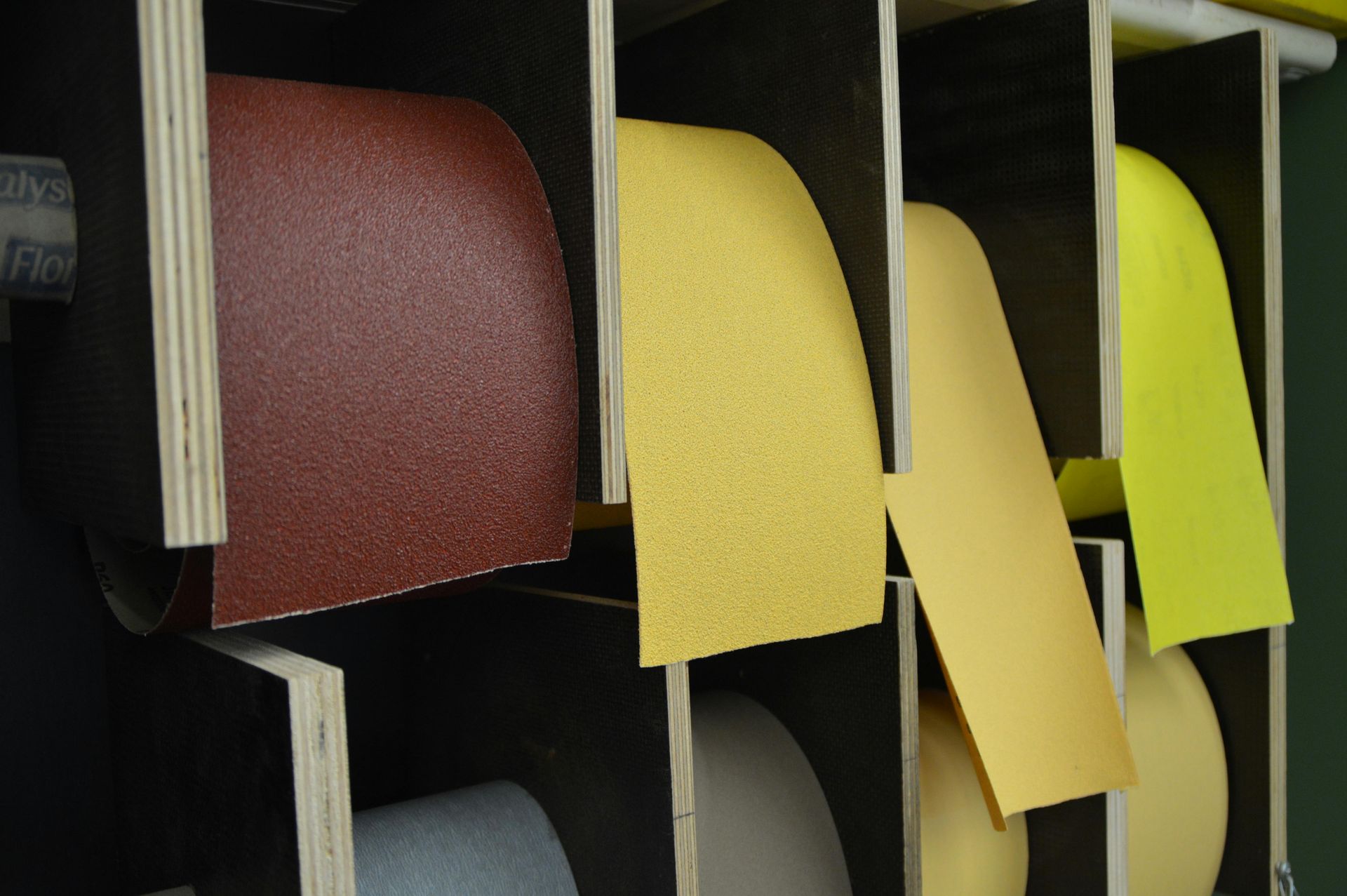 Shelves holding rolls of sanding belts in various colors: red, yellow, and tan.