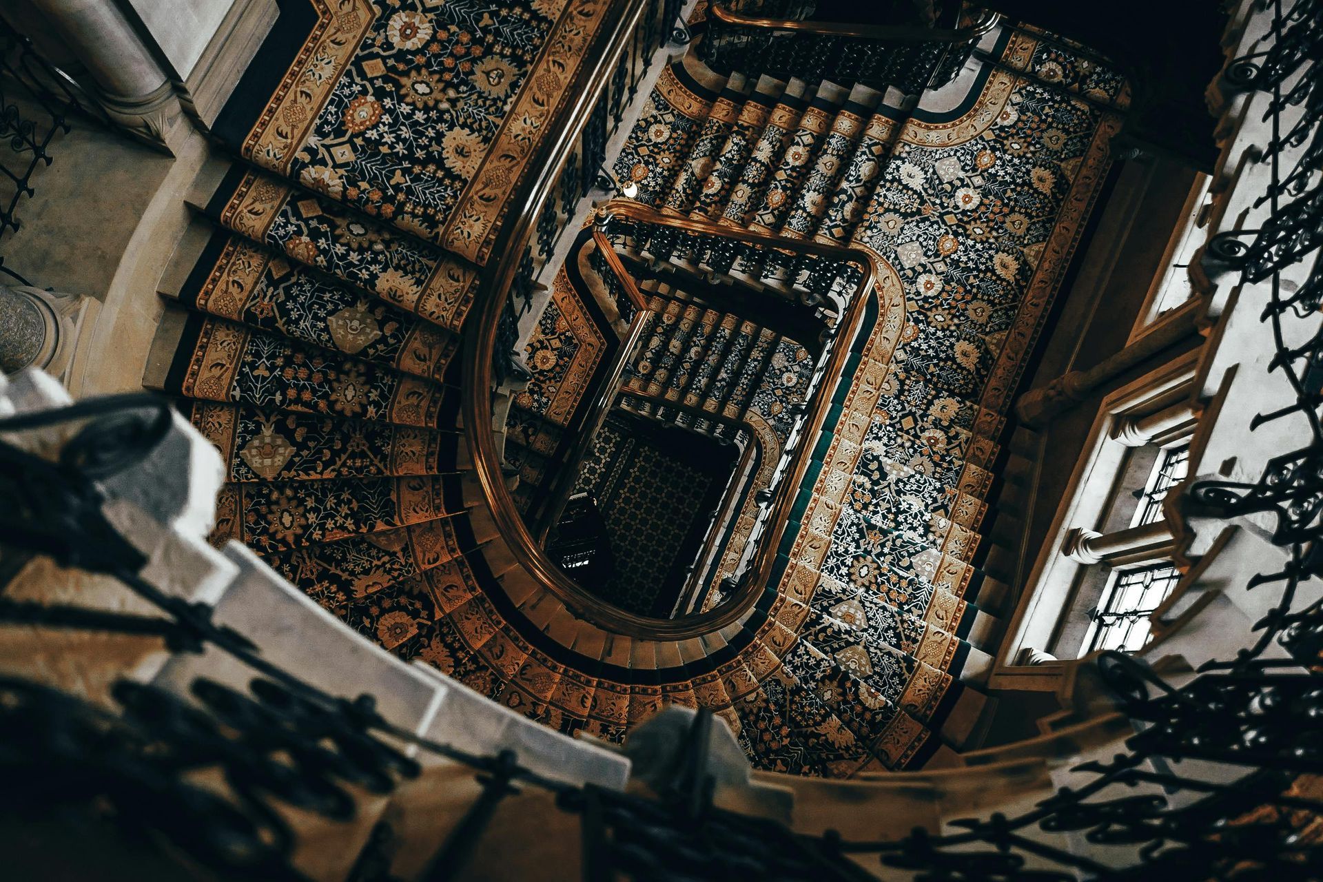 Spiral staircase, ornate carpet in shades of brown and blue, viewed from above, surrounded by windows.