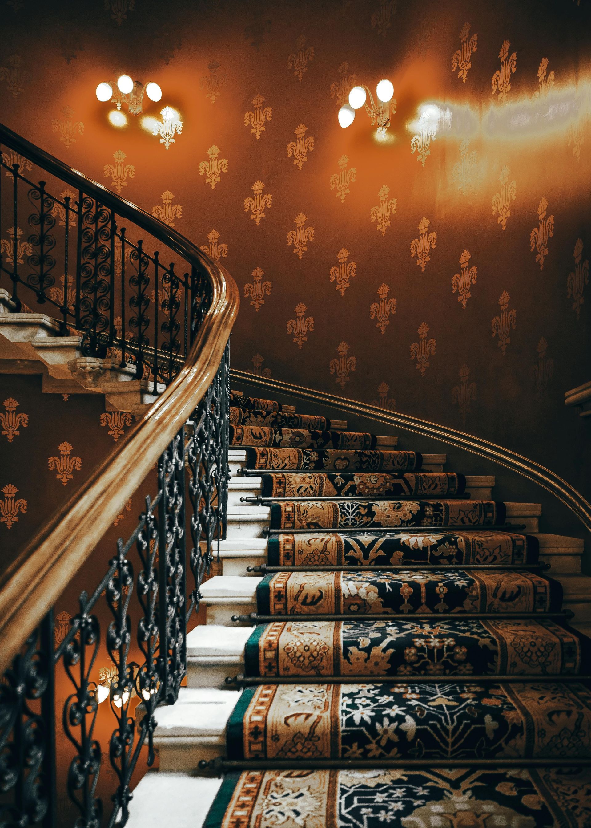 Ornate, curved staircase with patterned carpet and decorative railing. Warm, patterned wallpaper.