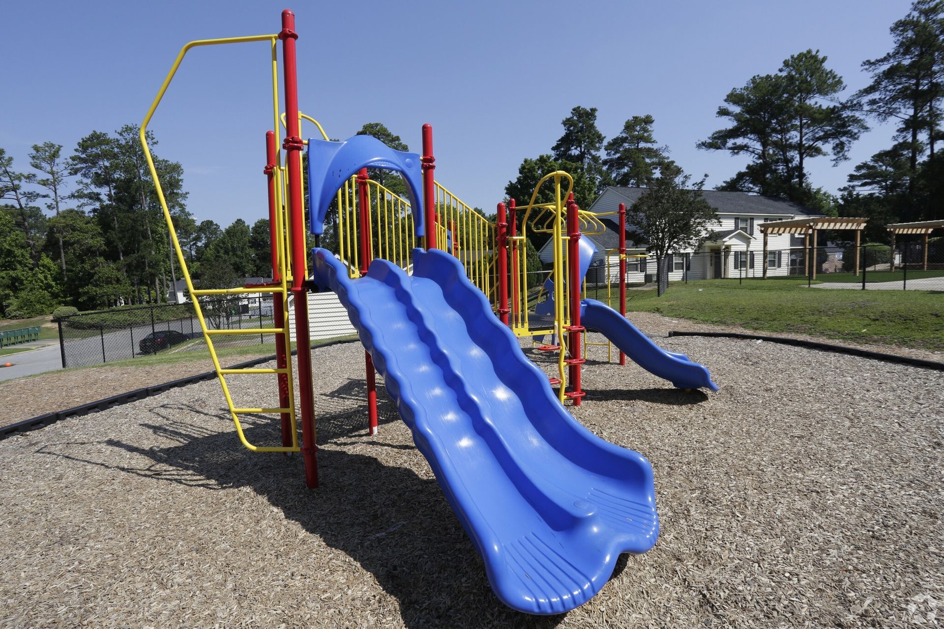 Playground with blue slides, red supports, and a yellow ladder on a sunny day.