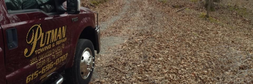 A red Putman Towing & Repair truck on a leaf-covered road.