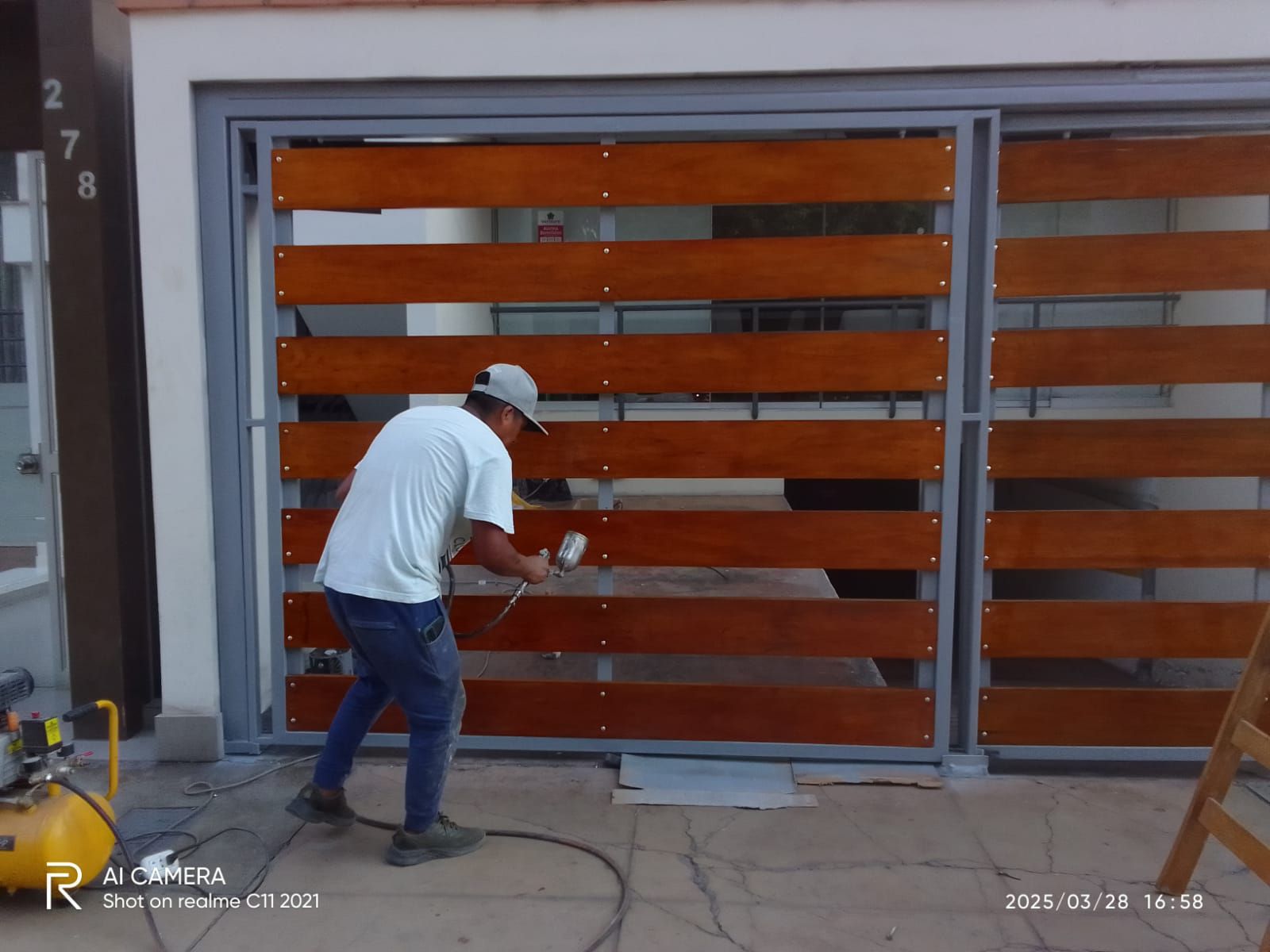 Hombre pintando con aerosol una puerta de madera con una mancha marrón afuera de un edificio.