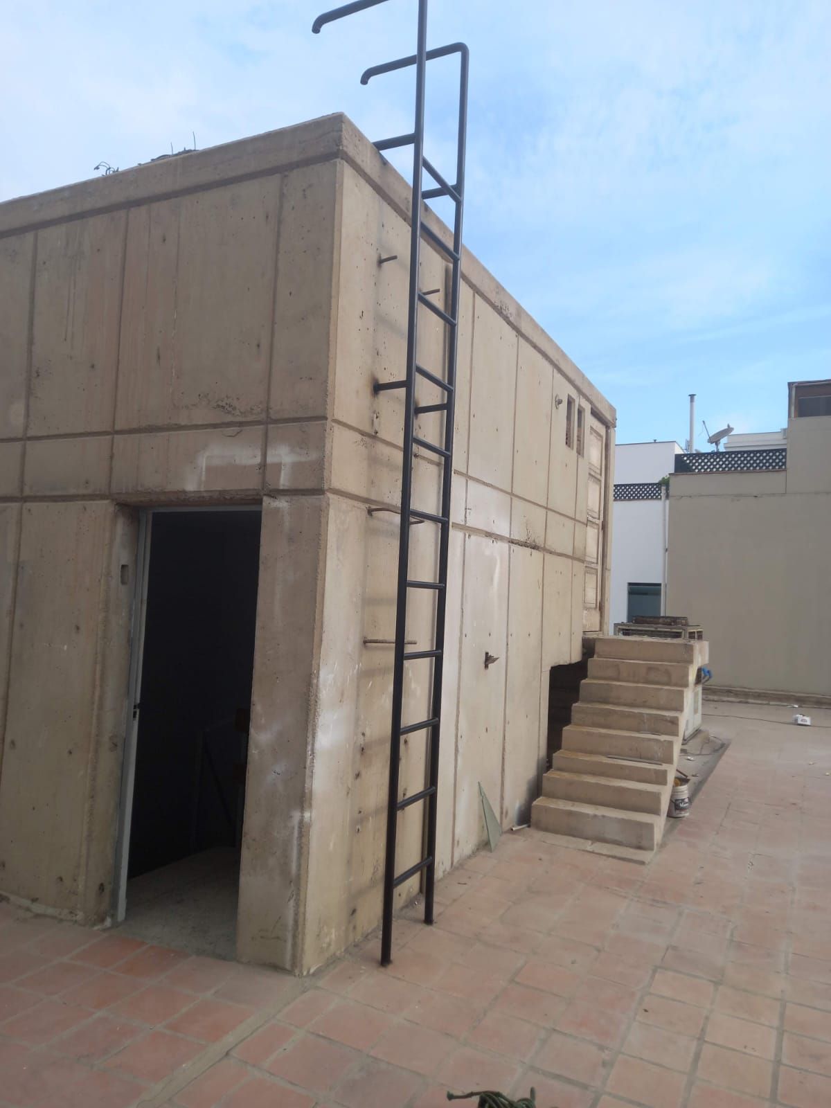 Escalera de metal negra en el lateral de un edificio de hormigón con puerta y escaleras abiertas.