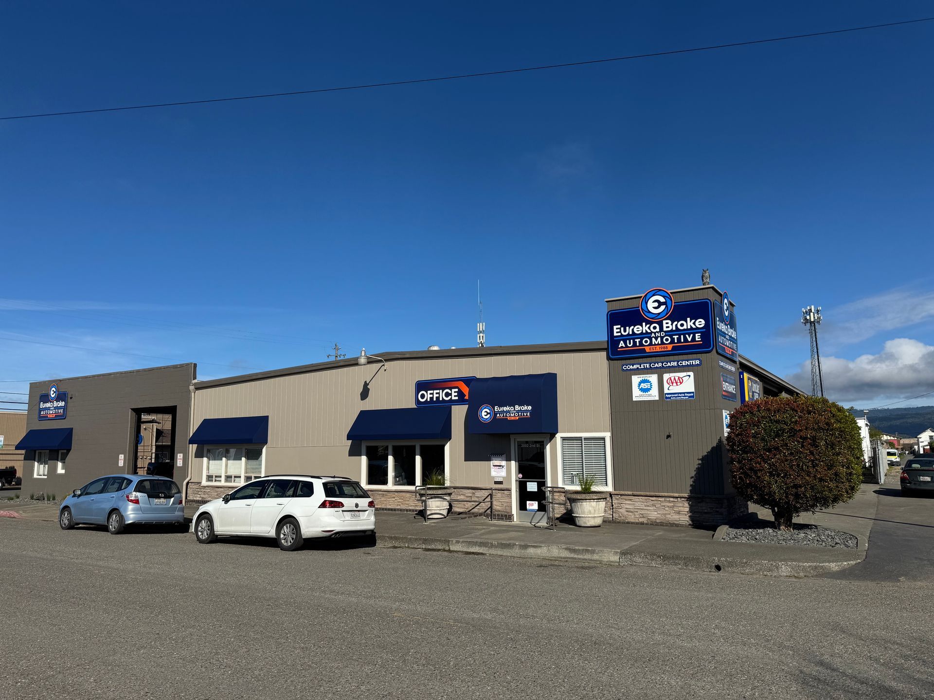 A beige commercial building with blue signage for Quality Auto Service under a clear blue sky, with cars parked in front | Eureka Brake and Automotive