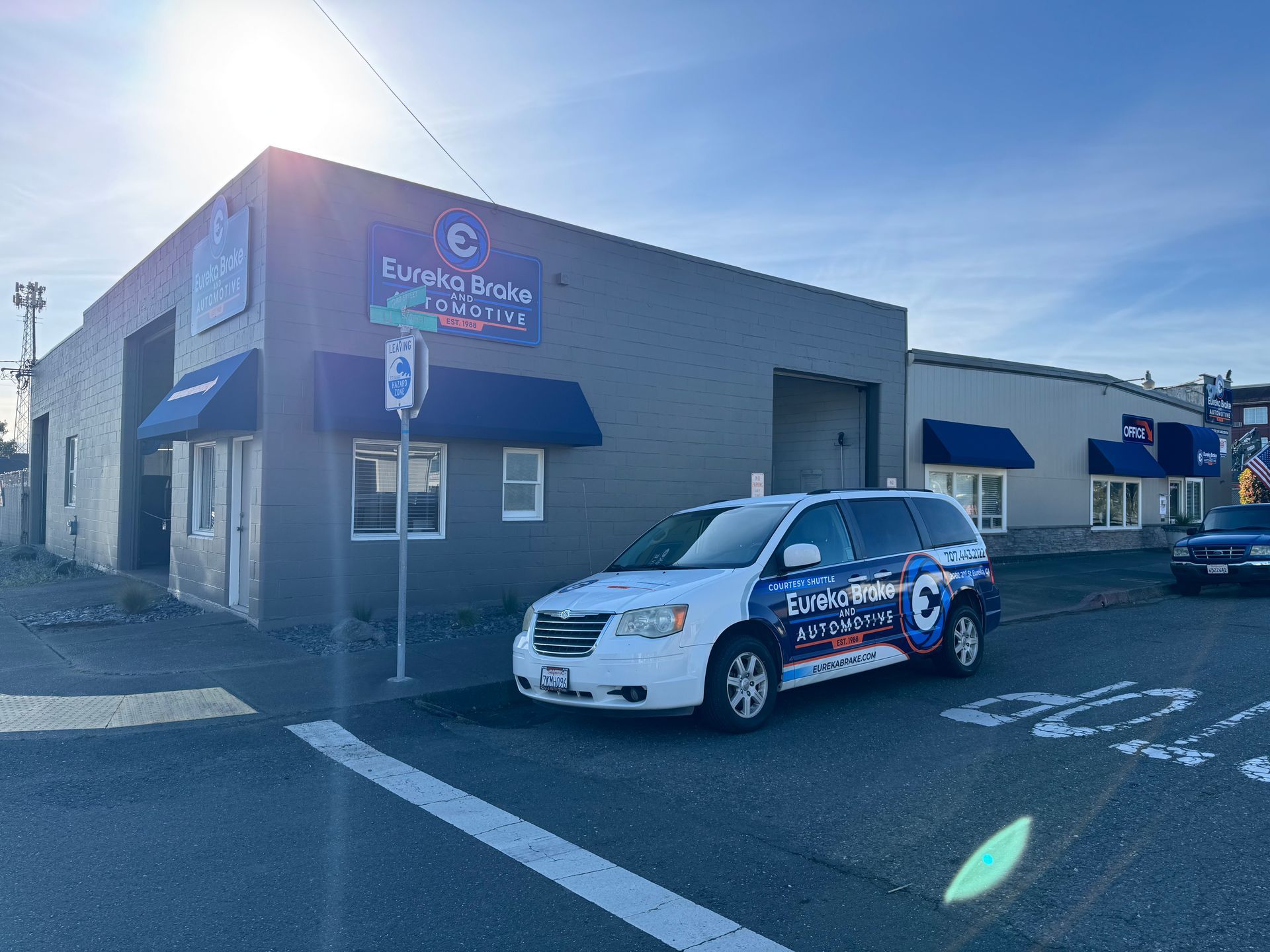 A blue and white branded van parked in front of a gray commercial building under a bright, sunny sky | Eureka Brake and Automotive