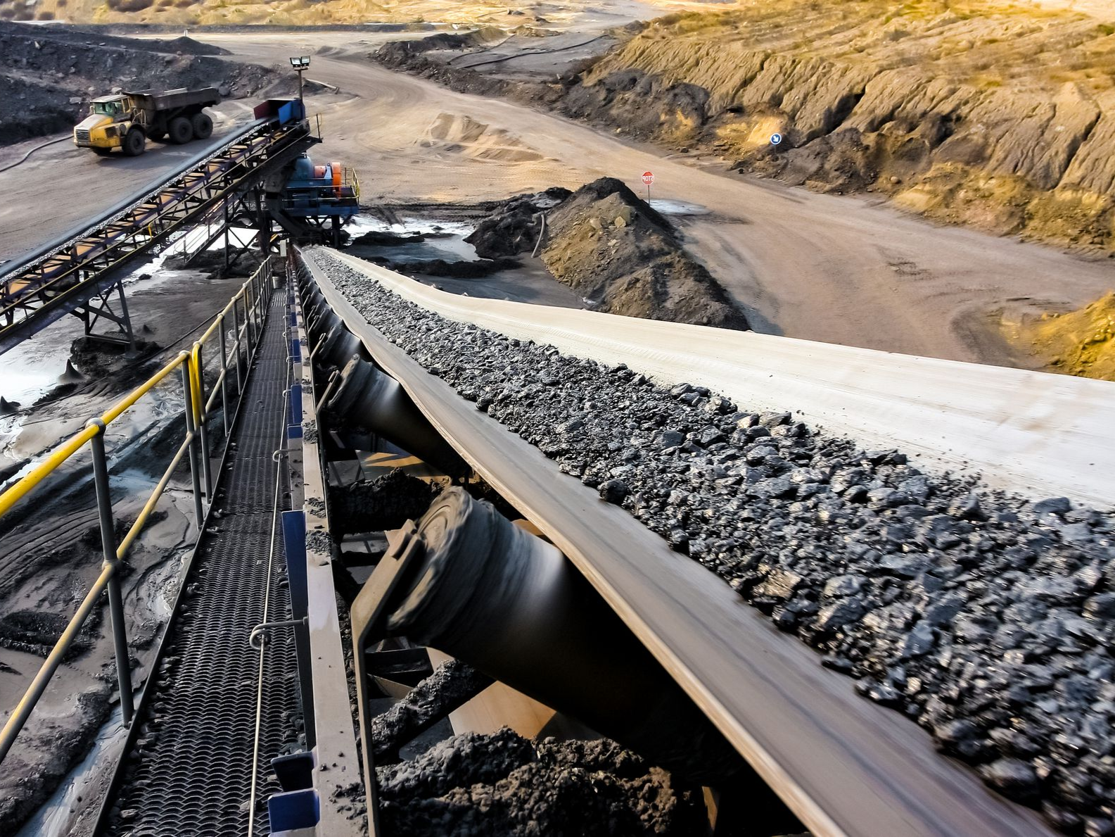 Open-pit mine conveyor carrying black rocks through a dusty quarry
