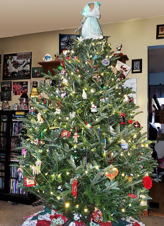 A christmas tree with a white angel on top is in a living room.
