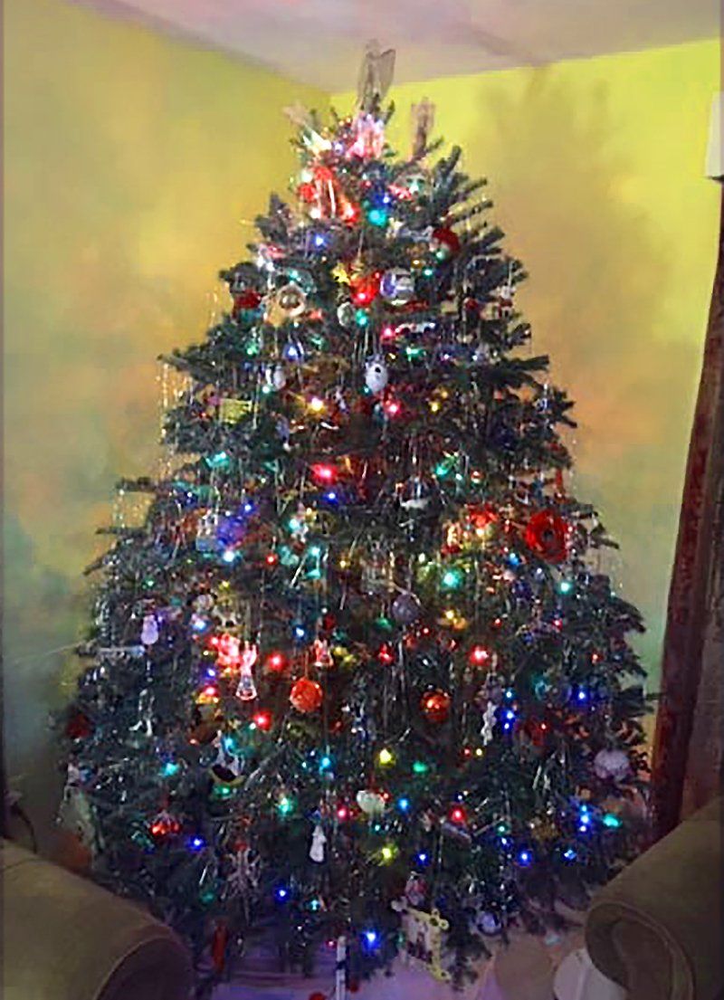 A christmas tree is sitting in a living room in front of a yellow wall.