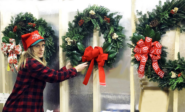 A woman is decorating a christmas wreath with a red bow.